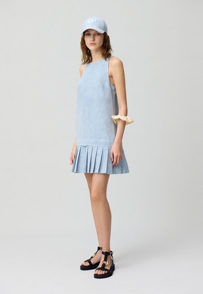 Robe sans manches bleu clair avec un ourlet plissé et des bords festonnés. Assortie d'une casquette assortie et de sandales à lanières noires.