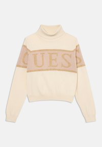 Maglione a collo alto crema con un design corto, caratterizzato da un logo "GUESS" in glitter dorato orizzontale sullo petto e polsini a coste.