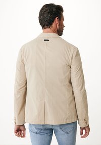 Beige, leichtgewichtige, einreihige Jacke mit Reverskragen, sichtbaren Nähten und zwei Knöpfen an den Manschetten. Glatte Textur.