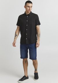Sort kortærmet skjorte med en lomme; stoffet ser let ud. Sammen med blå denimshorts og sorte sneakers. Enkel design.
