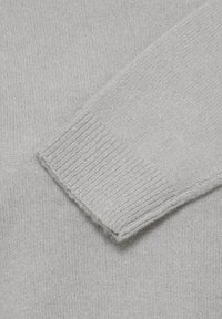 Tissu de pull en maille gris clair avec un gros plan sur un poignet côtelé d'une longue manche.