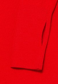 Punainen neulepaita, jossa on ribbikuvio ja sivureikä hihassa. Materiaali näyttää pehmeältä ja joustavalta.