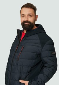 Granatowa kurtka puchowa z zamkiem błyskawicznym z przodu i kieszeniami, z czerwonymi akcentami, kapturem oraz strukturalnym materiałem. Regulowany krój z elastycznymi mankietami.