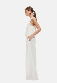 Top bianco senza maniche con design corto, abbinato a pantaloni bianchi a vita alta e lunghezza totale. Il tessuto sembra liscio e leggero.