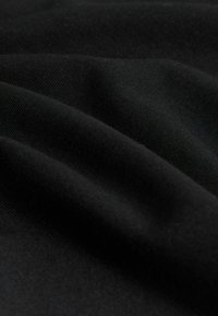 Tissu noir doux avec texture tricot visible et plis délicats créant des ombres et des reflets.