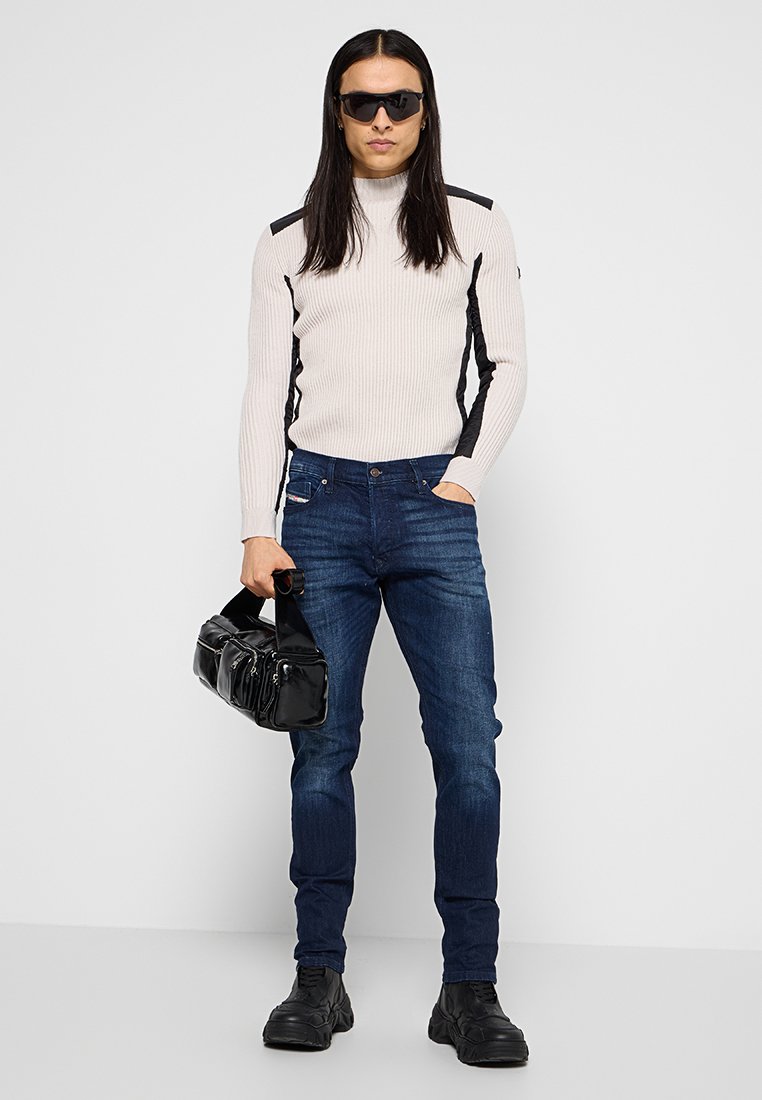 Chemise à manches longues gris clair à côtes avec des accents noirs sur les côtés, jean bleu marine, sac à main noir et lunettes de soleil, associée à des chaussures noires chunky.