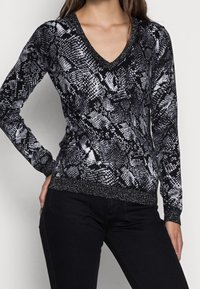 Pull-over à imprimé serpent noir et blanc avec un col en V, des manches longues et une bordure métallique texturée aux poignets et à l'ourlet.