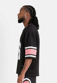 Jersey deportivo negro de manga corta con rayas rosas y blancas. Gran número blanco en el frente, hecho de material de malla transpirable.