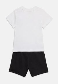 Λευκό T-shirt με κοντά μανίκια σε συνδυασμό με μαύρο σορτς, τοποθετημένο επίπεδα σε λευκό φόντο, παρουσιάζοντας την πίσω όψη της εμφάνισης.