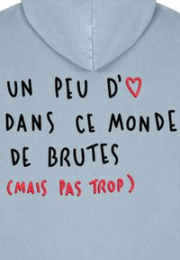Svijetlo plava dukserica s vezom u crnoj i crvenoj boji: "UN PEU D'❤️ DANS CE MONDE DE BRUTES (MAIS PAS TROP)."
