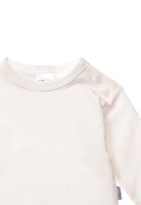 Helles Creme langärmliges Oberteil aus weicher Baumwolle, mit einem Rundhalsausschnitt und zwei Druckknöpfen auf der linken Schulter für ein einfaches Ankleiden.