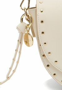 Borsa a tracolla color crema realizzata in materiale sintetico testurizzato, con borchie e accessori dorati, dotata di una tracolla regolabile e un'etichetta con il logo.