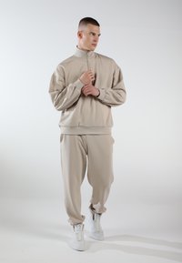 Beige sweatshirt with high collar and zip closure, paired with matching joggers. Made of soft fabric, features ribbed cuffs and side pockets.