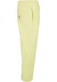 Pantaloni jogger de culoare galben deschis, cu o croială lejeră, având o textură moale și netedă, buzunare laterale și o etichetă logo neagră pe talie.