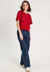 Top court en dentelle rouge avec des manches courtes, comportant des motifs floraux et un ourlet festonné, associé à un jean flare en denim foncé taille haute.