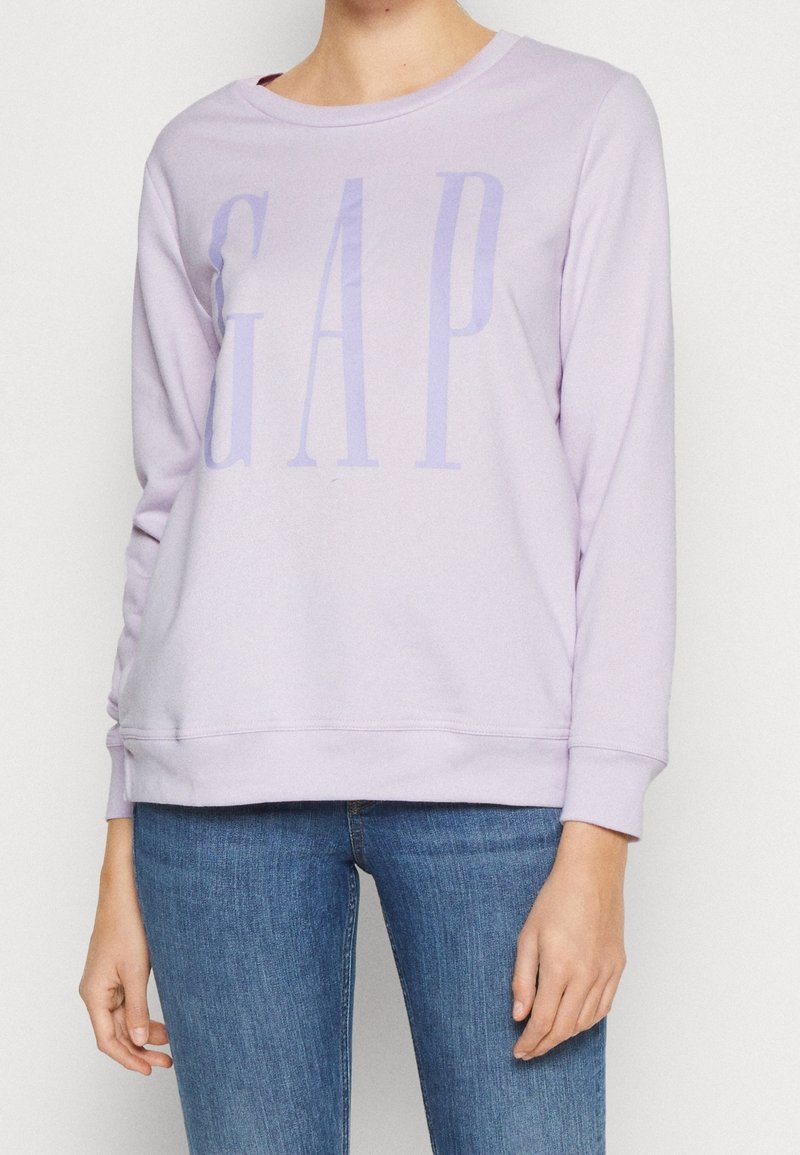 Felpa viola chiaro con logo "GAP" in una tonalità più scura. Presenta un collo rotondo, maniche lunghe e polsini a coste. Il materiale sembra morbido.