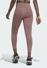 Leggings a vita alta, aderenti, di un morbido colore rosa, realizzati in materiale liscio ed elastico, abbinati a scarpe da ginnastica nere.