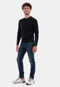 Maglione a maglia blu navy con texture a costine, abbinato a jeans di denim scuri. Le calzature presentano una base grigia chiara con accenti blu e arancioni.