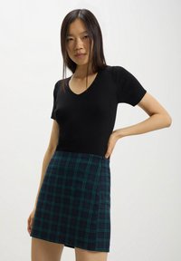 Top corto a maniche corte nero a coste con scollatura a V abbinato a una minigonna a quadri teal e blu navy, dotata di una zip laterale per la chiusura.
