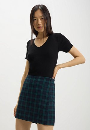 Top corto a maniche corte nero a coste con scollatura a V abbinato a una minigonna a quadri teal e blu navy, dotata di una zip laterale per la chiusura.