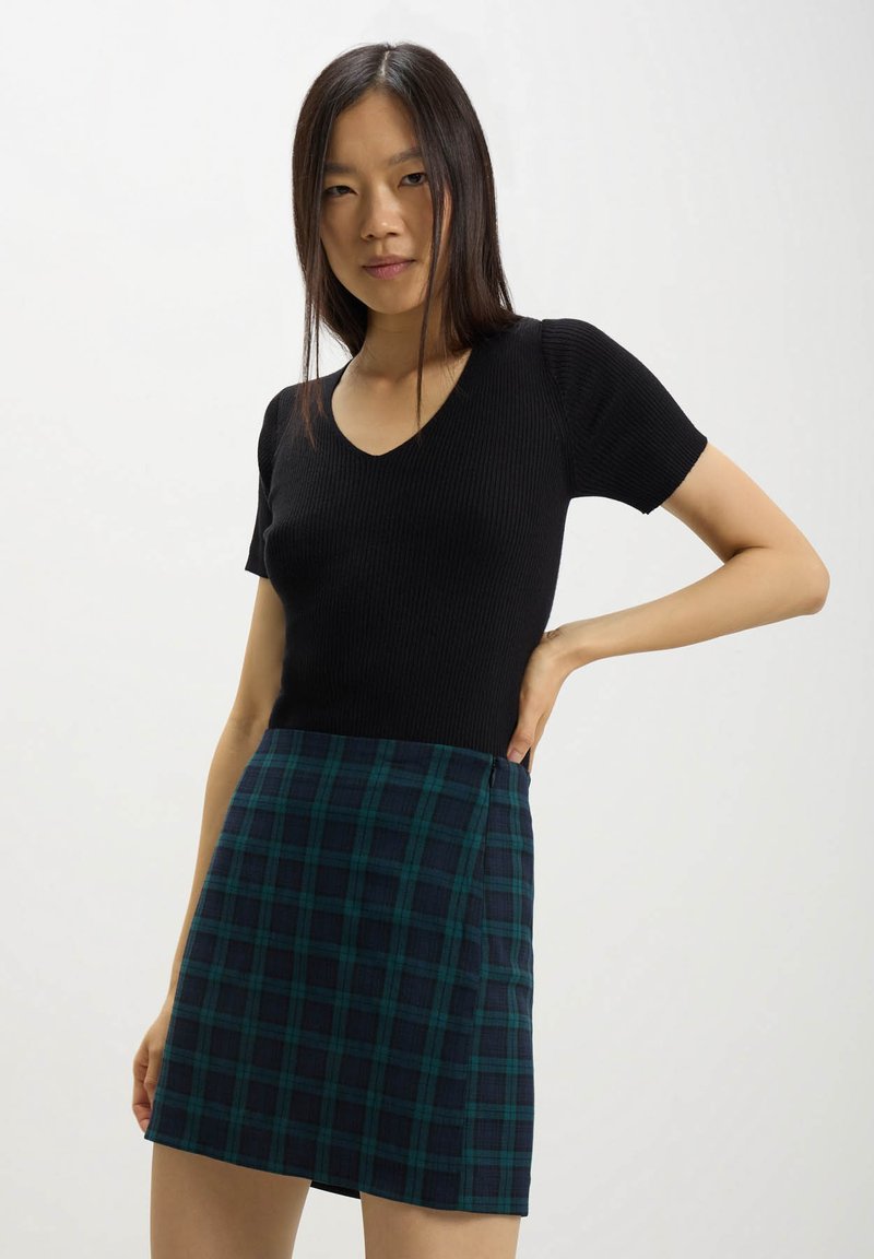 Top corto a maniche corte nero a coste con scollatura a V abbinato a una minigonna a quadri teal e blu navy, dotata di una zip laterale per la chiusura.