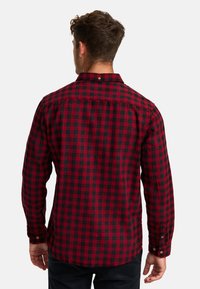 Camisa a cuadros en rojo y negro, con mangas largas, puños abotonados y cuello. Fabricada en una tela suave, presenta un pliegue en la espalda y un lazo para colgar.