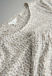 Top w serek w zwierzęcy wzór ze miękkiej tkaniny, z okrągłym dekoltem i kieszenią z plisami, w odcieniach beżu i jasnego brązu.