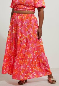 Jupe maxi dans un imprimé floral vibrante de rose et d'orange, fabriquée en tissu léger avec des volants superposés et une taille élastique.