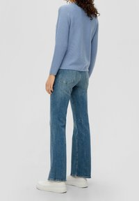 Lichtblauwe geribbelde trui, lange mouwen, gecombineerd met hooggersneden flared jeans en witte platform sneakers. Eenvoudig ontwerp, casual pasvorm.
