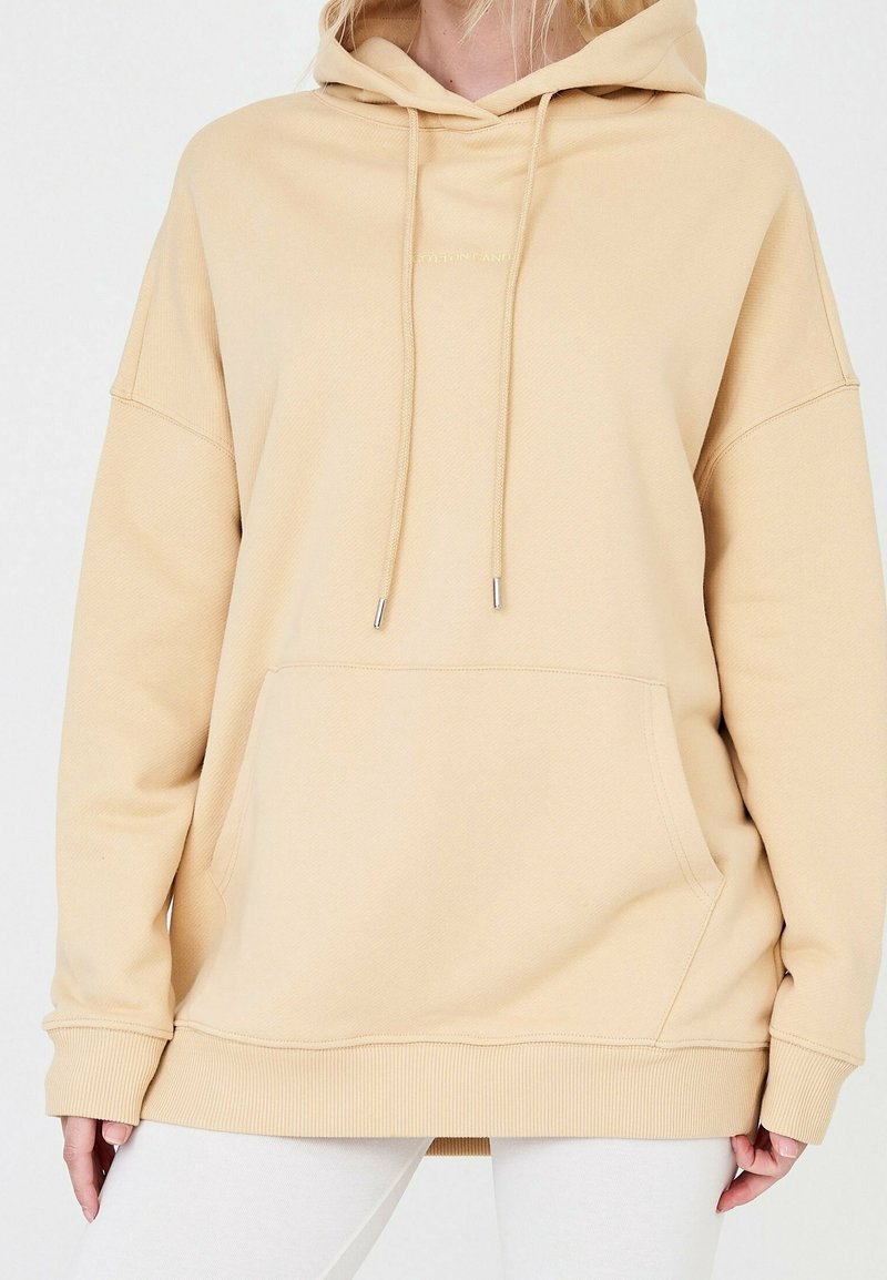 Béžová oversized mikina z bavlněné směsi, s předním kapsou, stahovací kapucí a žebrovanými manžetami a lemem. Jednoduchý, texturovaný design.