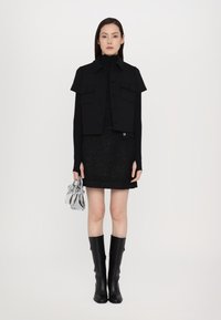 Gilet nero corto con maniche corte, dolcevita nero sotto, gonna nera a trama, borsa lucida argento e stivali al ginocchio neri.