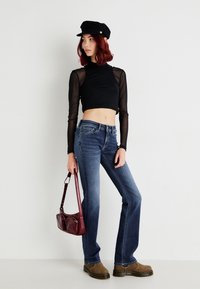 Zwart cropped langmouwen top met doorzichtige mouwen, blauwe flared jeans, bruine platform laarzen en een bordeauxrode handtas. Een zwarte pet maakt de look compleet.