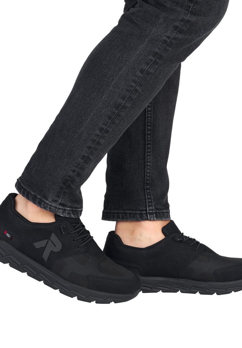 Chaussures de sport noires avec des détails en mesh, un tissu lisse et une semelle texturée. Lacets noués et logo affiché de manière proéminente sur le côté.