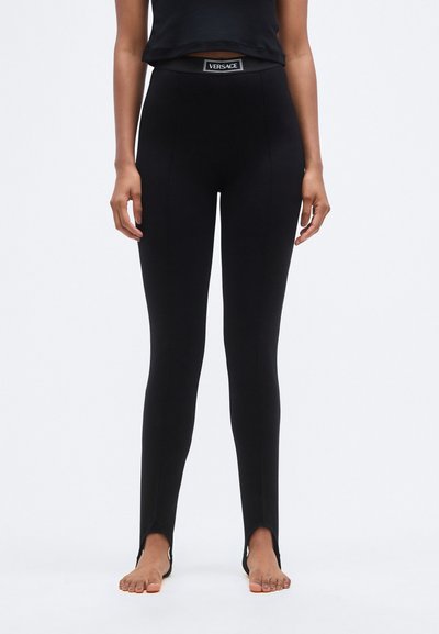 Leggings noirs à coupe ajustée, avec une taille haute et des fentes aux chevilles, agrémentés d'une étiquette de marque à la taille. Texture lisse.