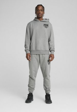 Hanorac gri și pantaloni asortați dintr-un material moale, cu un logo pe piept și pe coapsă. Pantalonii au manșete elastice și buzunare laterale.