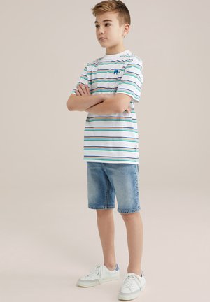 Vit kortärmad randig t-shirt med gröna och blå linjer, matchad med ljusa denimshorts och vita sneakers med blå akcenter.