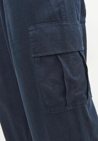 Pantalons cargos de la marine en tissu doux, avec des poches latérales, une coupe décontractée et des détails cousus le long des coutures et des poches.