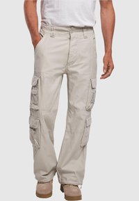 Beige cargo kalhoty s několika bočními kapsami, elastickým pasem a volným střihem; spárované s hnědými botami a bílým tričkem.