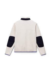 White fleece jacket with navy elbow patches and collar, featuring a minimalist design and contrasting blue trim along the hem.