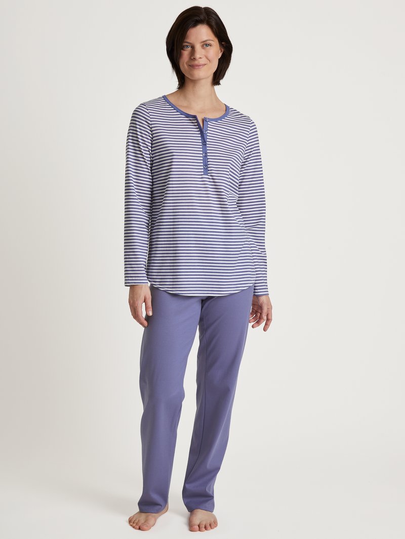 Gestreiftes Langarmshirt in Marineblau und Weiß mit einem Fünf-Knopf-Verschluss, kombiniert mit einfarbigen lila Hosen, die aus weichem Stoff gefertigt sind.
