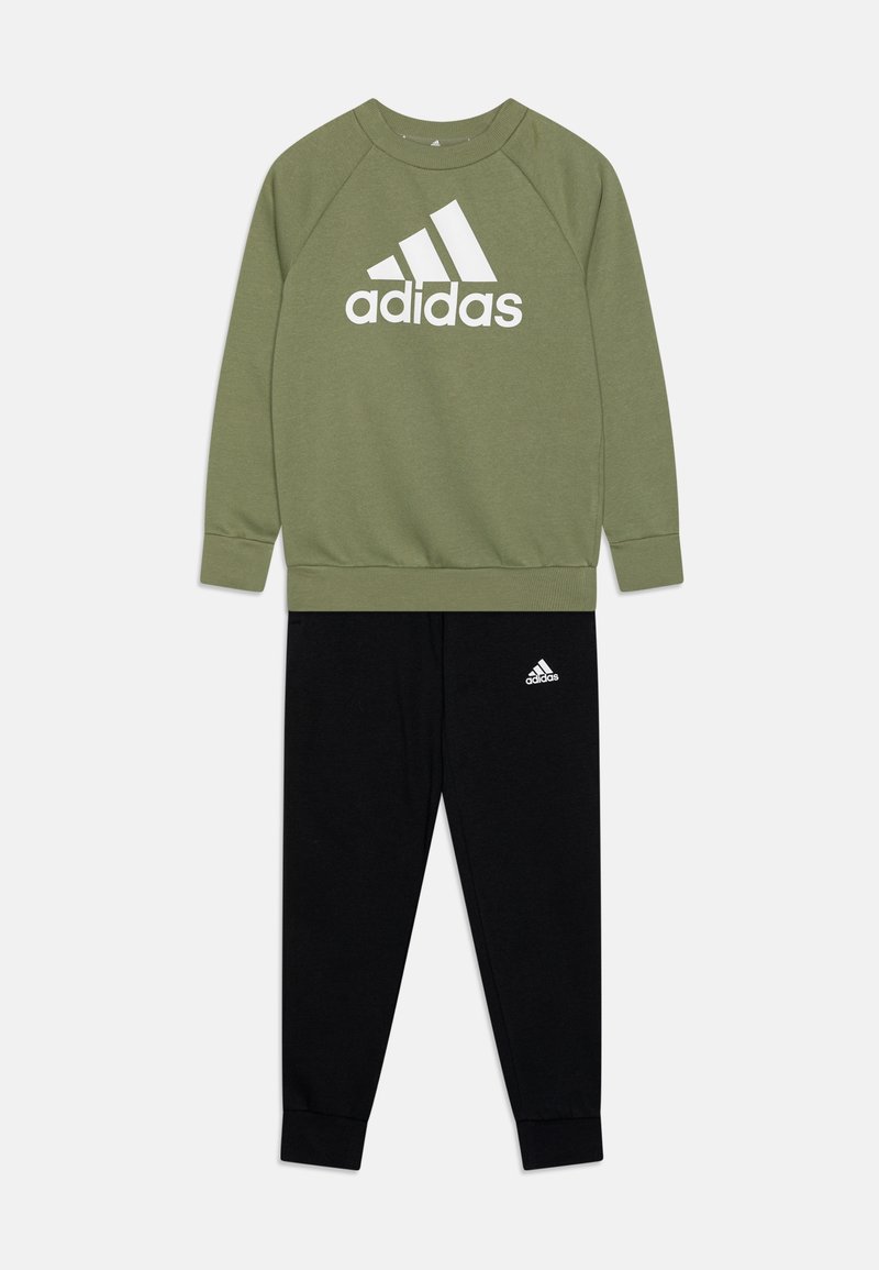 Sudadera verde oliva con el logo blanco de "adidas", combinada con pantalones de chándal negros que tienen un pequeño logo blanco. Ambos tienen una textura suave.