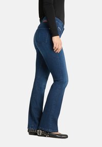 Jeansy dzwony z denimu w ciemnym niebieskim kolorze o gładkiej fakturze, z talią na wysokości środkowej, pięcioma kieszeniami i lekko spranym wykończeniem na nogawkach.