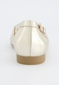 Zlaté metalické ploché boty se zaoblenou špičkou a nízkým hnědým gumovým podpatkem; mají malou sponu na boku a hladký povrch.