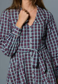 Röd, blå och grön rutmönstrad klänning med V-ringning, knappar framtill och långa puffärmar. Inkluderar knytband i midjan och en plisserad kjol.