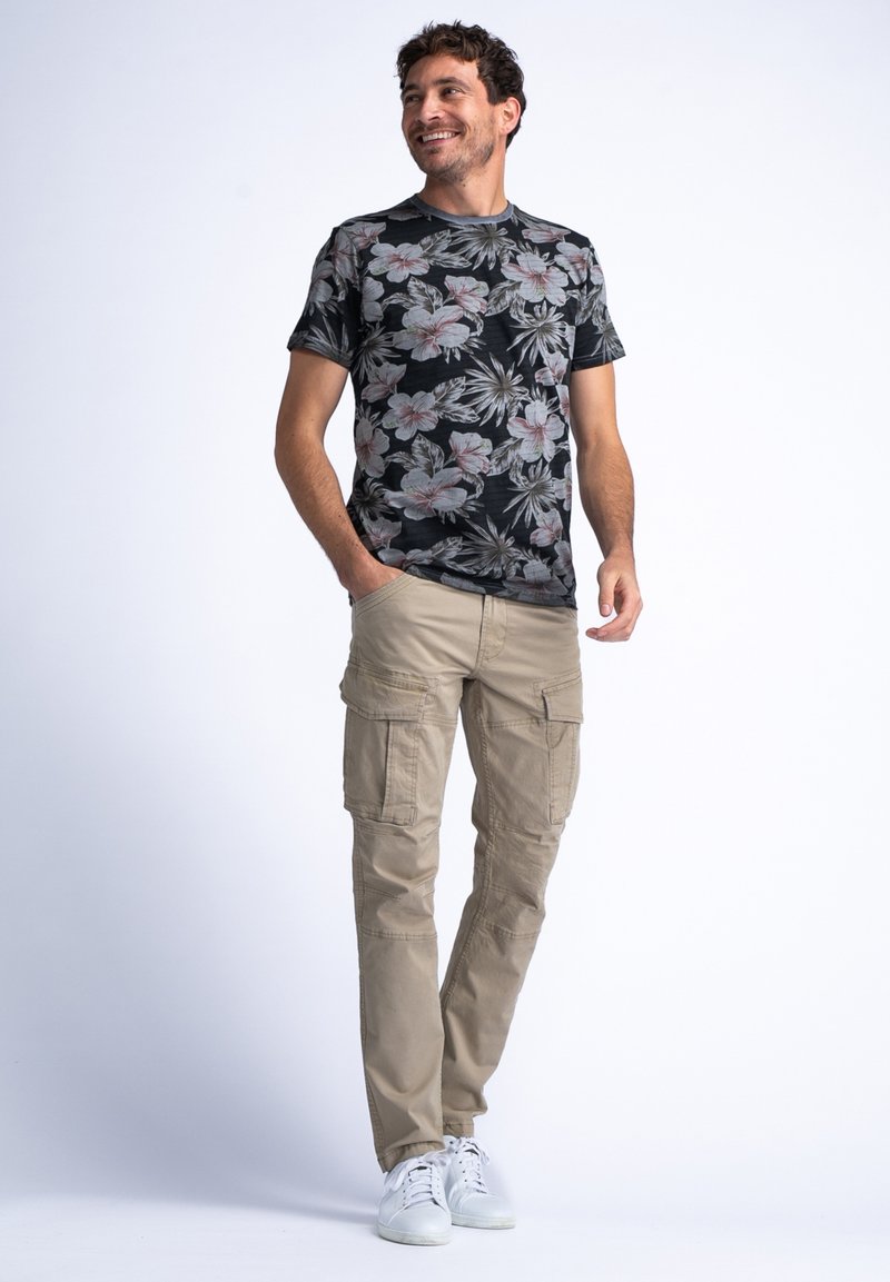 Camisa corta de flores negras con patrones en rosa y verde, combinada con pantalones cargo beige que tienen múltiples bolsillos y zapatillas blancas.