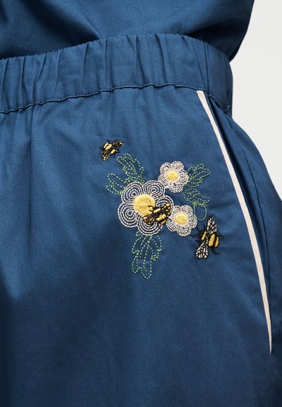 Μπλε παντελόνι ύφασμα με κεντημένα κίτρινα και λευκά λουλούδια και τρεις μέλισσες κοντά σε ελαστική μέση και λευκή πλευρική ρίγα.