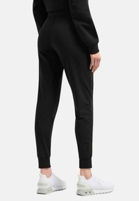 Pantaloni da jogging neri con vita elasticizzata e caviglie a costina, realizzati in tessuto liscio. Abbinati a scarpe da ginnastica bianche.