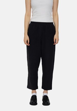 Black linen cropped pants with an elastic waistband, featuring a relaxed fit and a smooth texture. Paired with black shoes and white socks.
