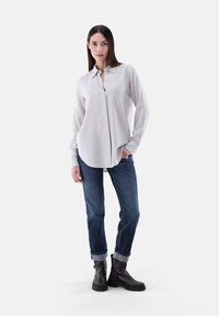 Hellgraues Hemd mit Knopfleiste, langen Ärmeln, weicher Stoff, kombiniert mit dunkelblauen Denim-Jeans, aufgerollten Bündchen und schwarzen Ankle Boots.