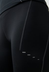 Zwarte sportleggingen gemaakt van rekbaar materiaal met een zichtbare zijnaad en een reflecterende accent in een lijnpatroon.